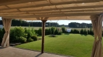 Cortina impermeable a medida instalada en una pérgola de jardín beige con vistas al césped y al bosque.