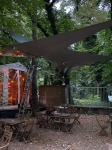 Vodootporno trokutasto jedro za zaštitu od sunca po mjeri postavljeno iznad stolova u šumskom vrtu restorana.