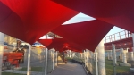 Red premium waterproof shade sail in a triangle shape, mounted over a path as a terrace and garden canopy.