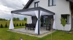 Witte zijgordijnen voor pergola in set voor houten constructie op terras met tuinmeubilair.