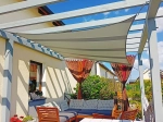 Velă de umbră impermeabilă premium 3x4,5 montată deasupra unei terase cu mobilier de grădină și pergolă.
