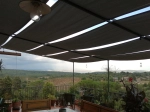 Toldo lateral impermeable 0,7x5 fijado a estructura metálica en terraza con vistas al bosque y viñedos.