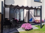 Store romain horizontal premium sous une pergola sur une terrasse avec meubles de jardin et fleurs. Toit de terrasse pliable.
