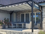 Store romain horizontal gris premium Decor sur une pergola noire au-dessus de meubles de jardin sur une terrasse.
