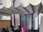 Γκρι οριζόντια premium Decor ρωμαϊκή κουρτίνα σε βεράντα πάνω από μαύρο σετ επίπλων κήπου και λουλούδια.