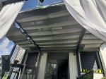 Οριζόντιο ρωμαϊκό στόρι premium Decor 2,5x3 m τοποθετημένο σε γραφίτη πέργκολα βεράντας με λευκές κουρτίνες.