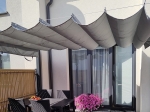 Siva horizontalna rimska zavesa premium Decor nad teraso z vrtnim pohištvom in cvetjem.
