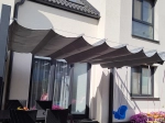Γκρι οριζόντιο premium ρωμαϊκό στόρι Decor 3x4 m τοποθετημένο πάνω από τη βεράντα δίπλα σε έπιπλα κήπου και κούνια.