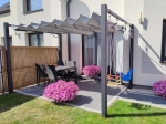 Γκρι-μπεζ οριζόντιο ρωμαϊκό στόρι premium Decor 3x4 τοποθετημένο σε γραφίτη πέργκολα πάνω από σετ τραπεζαρίας βεράντας.