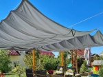 Vela de sombra retrátil impermeável cinzento claro 2,5x4 m sobre terraço com móveis de jardim sob um céu azul.
