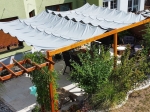 Γκρι αδιάβροχο επεκτεινόμενο πανί σκίασης 2,5x5 m τοποθετημένο σε ξύλινη πέργκολα στον κήπο πάνω από έπιπλα εξωτερικού χώρου.