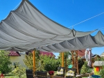 Grey garden sail waterproof retractable 3x3 m mounted over a wooden pergola with a set of garden furniture.