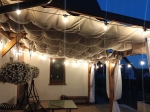 Retractable waterproof sail shade 3x3 m in beige, installed on a terrace with atmospheric string lighting.