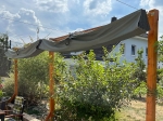 Γκρι, αδιάβροχο επεκτεινόμενο πανί σκίασης 3x3 τοποθετημένο σε ξύλινη κατασκευή σε έναν ηλιόλουστο κήπο.
