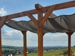 Vela de sombra de deslizar impermeável 3x3 cinzenta, montada numa pérgola de madeira com vista para a paisagem.