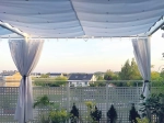 Vela de sombra branca impermeável retrátil 3x3 m instalada num terraço com vista para casas e jardins.