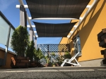Γραφίτης πανί σκίασης HDPE 5x5 τοποθετημένο σε βεράντα πάνω από ξύλινες γλάστρες και μια λευκή ξαπλώστρα.