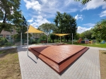 Žltá trojuholníková tieniaca plachta HDPE 5x5x7 zakrývajúca drevené pódium na modernom ihrisku.