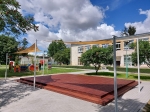 Vela ombreggiante triangolare HDPE 6x6x6 che ombreggia una pedana in legno in un parco giochi scolastico.