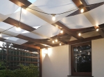 Faixa de sombra clara personalizada para pavilhão cobrindo uma pérgula de madeira com iluminação decorativa.