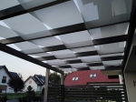 Light custom-made sunshade sail, interwoven through the beams of a modern dark pergola on a terrace.