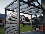 Toldo vela gris y blanco 0,75x5 m entrelazado entre las vigas de madera de una pérgola de terraza.