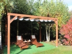 Horizontale PVC-Faltmarkise an einer Holzpergola über Gartenliegen, umgeben von Bäumen.