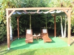 Horizontaal PVC vouwgordijn op maat gemaakt, gemonteerd op een houten pergola met tuinligstoelen op de achtergrond.