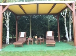 Op maat gemaakt houten PVC terrasoverkapping voor het hele jaar met twee ligbedden en tafels in een bostuin.
