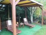 Op maat gemaakt PVC-terrasoverkapping voor alle seizoenen op een houten constructie met ligstoelen op de achtergrond.