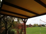 PVC terrasoverkapping op maat voor het hele jaar met solide constructie, uitzicht op de tuin met sportveld en houten prieel.