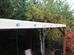 Wit jaarrond terrasdak van PVC met montageogen, geïnstalleerd op een houten constructie in de tuin.
