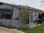 Transparente Terrassenverkleidung nach Maß aus grauer Plane mit Fenster, schützt Gartenlaube vor Wind.