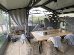 Fermeture de terrasse transparente sur mesure installée dans une pergola moderne avec mur en pierre et table en bois.