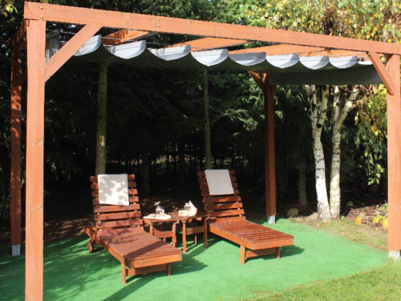 Horizontaal PVC vouwgordijn op maat gemonteerd op een houten pergola boven ligbedden.