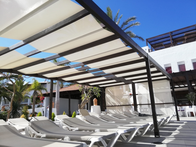 Espace de détente avec transats abrités par un store romain blanc sur mesure installé sur une pergola.