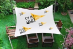 Çim üzerindeki ahşap bahçe mobilyalarının üzerinde SUNSHADE grafikli kişiye özel su geçirmez reklam yelkeni.