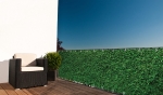 Op maat gemaakte balkonafscherming met groen bladerenmotief, gemonteerd op een terrasreling met tuinmeubilair.