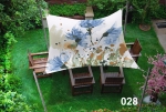 Waterdicht schaduwdoek op maat met blauwe bloemenprint boven houten stoelen op het gazon.