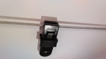 Black plastic stopper for slide sails and Roman blinds, mounted on a steel cable against a white wall.