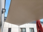Vela de sombra beige impermeable a medida para balcón instalada sobre terraza, protege del sol y la lluvia.