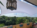 Toldo vela rectangular blanco impermeable a medida instalado en una terraza con vistas al parque.