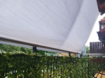 Weißes wasserdichtes Balkon-Sonnensegel nach Maß über einem mit einer Hecke abgeschirmten Geländer.