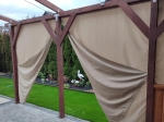 Beige vandtæt havegardin efter mål monteret på en træpavillon med havebaggrund.