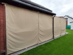 Rideau de jardin imperméable sur mesure installé sur une terrasse en bois, tissu extérieur beige protégeant de la pluie.