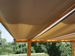 Αδιάβροχη μπεζ λωρίδα κιόσκι 0,5x5 m τοποθετημένη σε ξύλινη πέργκολα παρέχει σκιά και προστασία από τη βροχή.