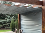 Οριζόντια ρωμαϊκή κουρτίνα premium Decor διαστάσεων 2,5x3 m τοποθετημένη σε ξύλινη πέργκολα στον κήπο.