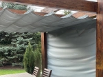 Store romain horizontal premium Decor de 2,5x3 m monté sur une pergola en bois dans un jardin.