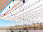 Weißes horizontales Premium-Faltrollo Decor 3x3 beschattet eine sonnige Terrasse mit bunten Lichterketten.