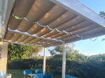 Οριζόντια ρωμαϊκή ρολέτα premium Decor 3x4 σε πέργκολα βεράντας προσφέρει σκιά πάνω από μπλε έπιπλα κήπου.
